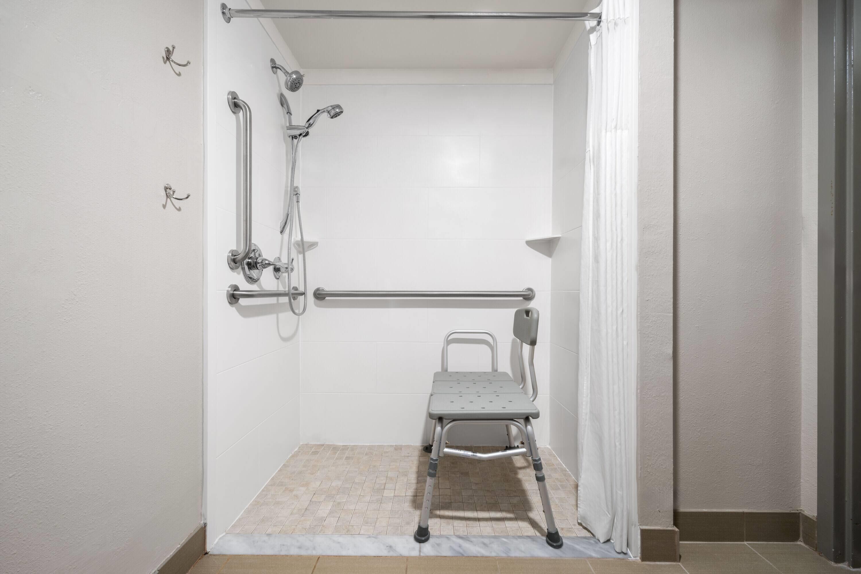 A shower area with a grab bar, a showerhead, and a shower seat.