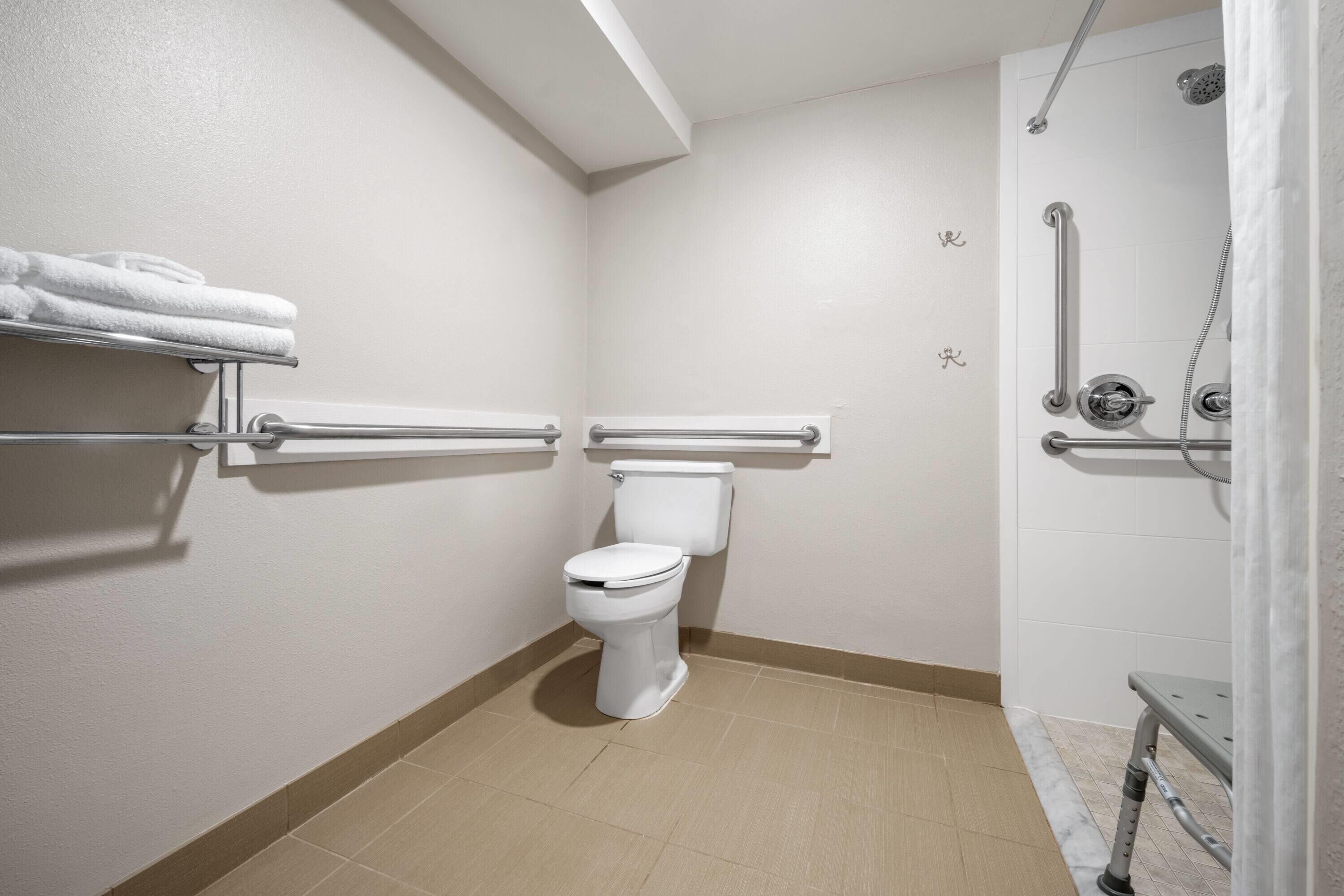 A bathroom with a toilet, grab bars, a shower area, and a towel rack.