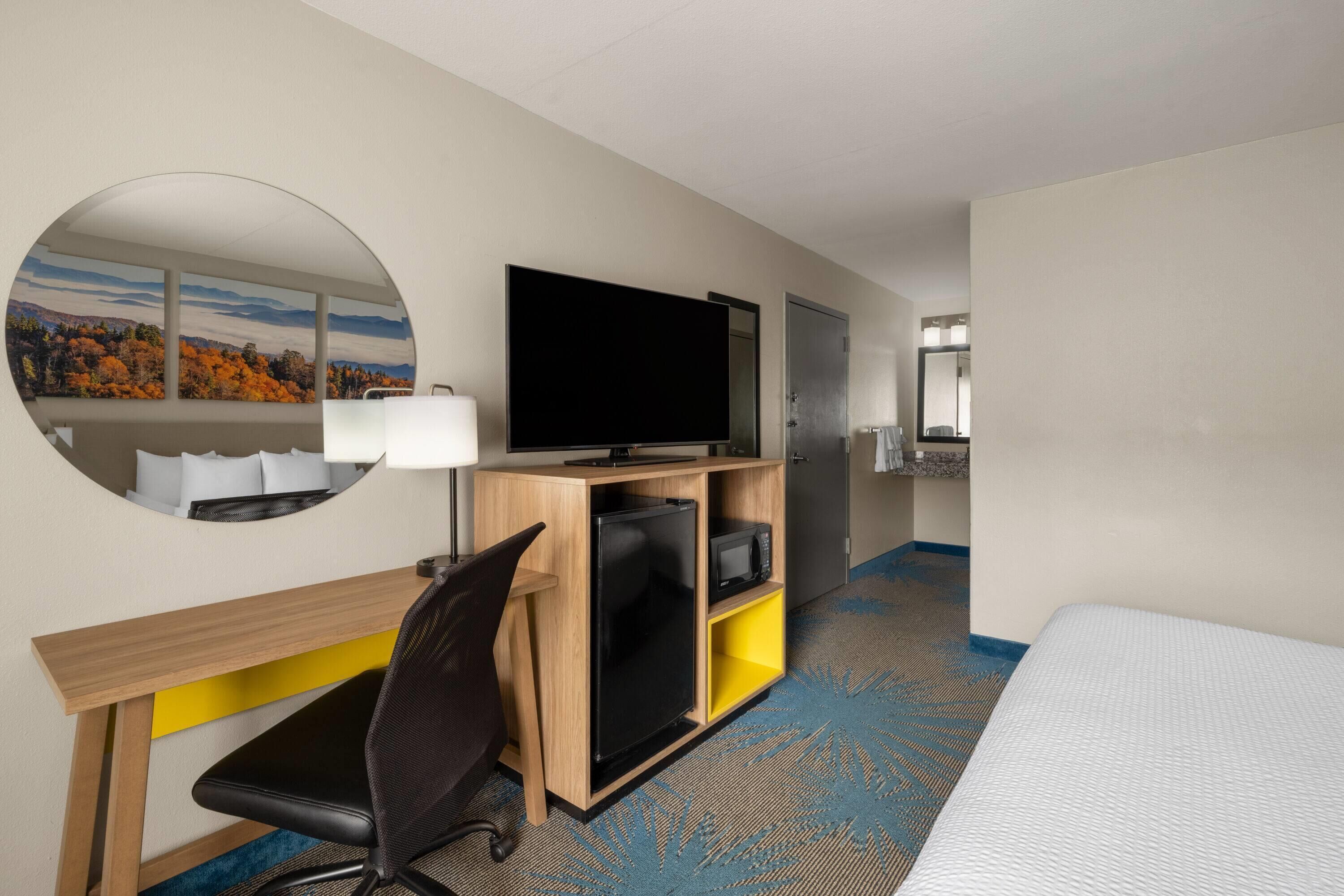 Hotelkamer met een bed, bureau met flatscreen televisie, spiegel en uitzicht op herfstbomen.