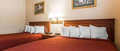 Una habitación de hotel con dos camas, una mesita de noche, una lámpara y dos cuadros en la pared.