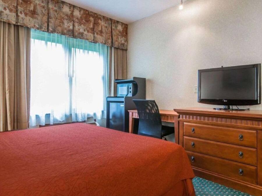 A hotel room with a bed, a desk with a television, a microwave, and a chair.