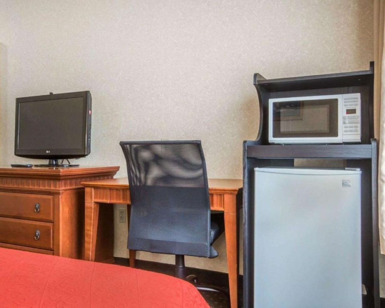 A hotel room with a bed, a desk with a computer monitor, a microwave, and a refrigerator.