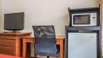 Una habitación de hotel con cama, un escritorio con monitor de computadora, un microondas y un refrigerador.