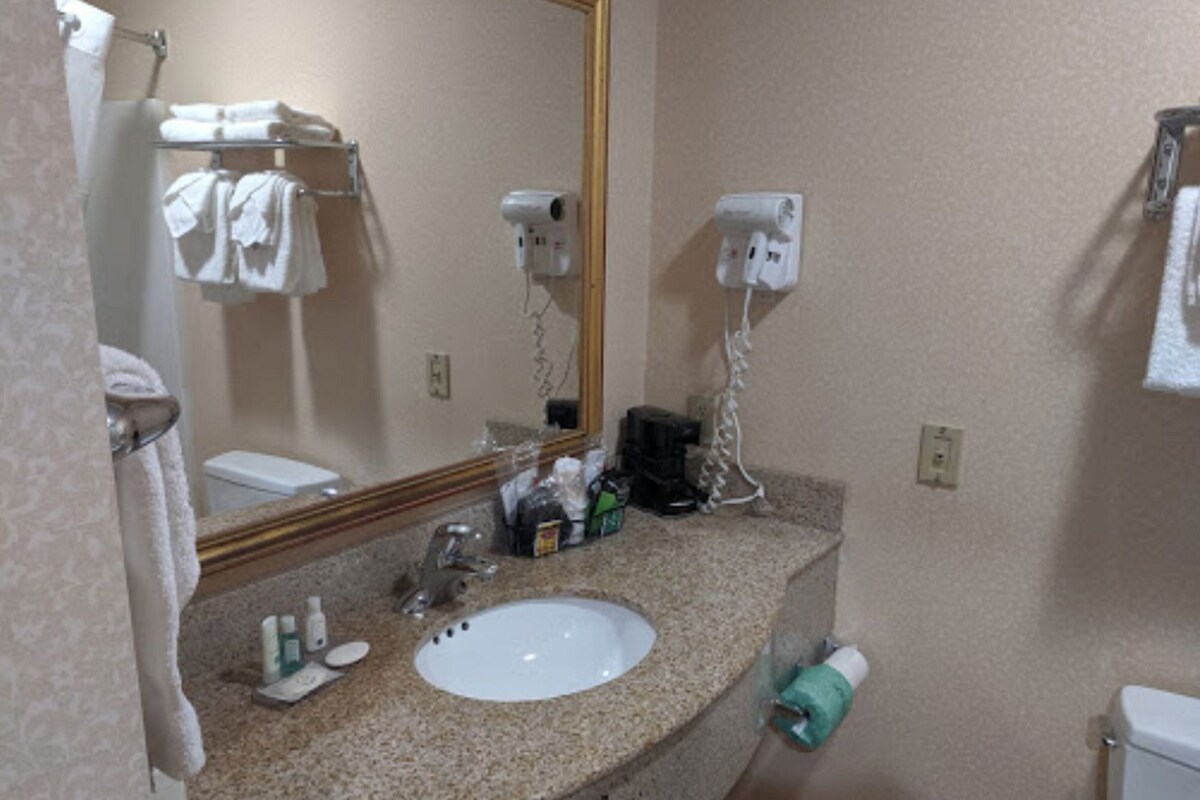 A bathroom with a sink, mirror, towel rack, hair dryer, and toiletries.