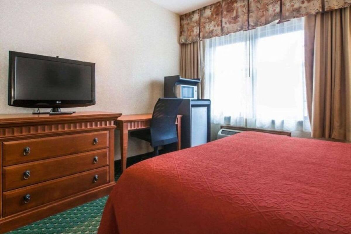 Una habitación de hotel con cama, televisión, escritorio con silla, cómoda y ventana con cortinas.