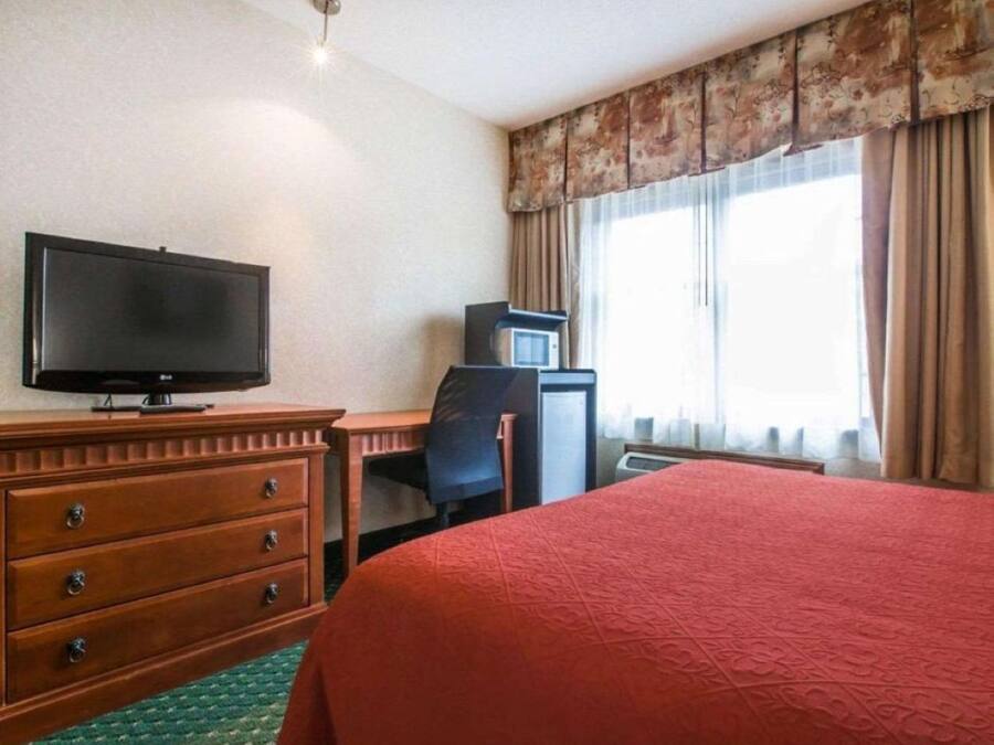 A hotel room with a bed, a TV, a desk with a chair, a dresser, and a window with curtains.