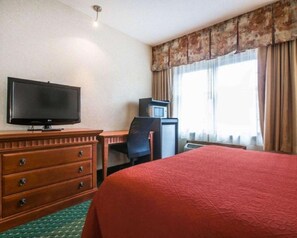 A hotel room with a bed, a TV, a desk with a chair, a dresser, and a window with curtains.