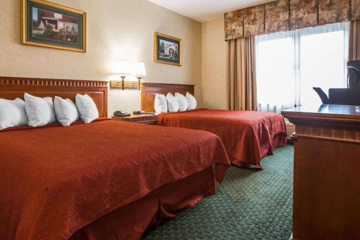 Habitación de hotel con dos camas, un escritorio, una silla, una lámpara y dos cuadros en la pared.