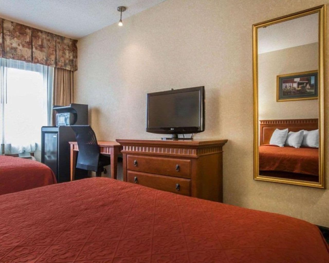 Une chambre d’hôtel avec deux lits, une télévision, un bureau avec une chaise et une commode.