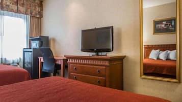 Une chambre d’hôtel avec deux lits, une télévision, un bureau avec une chaise et une commode.