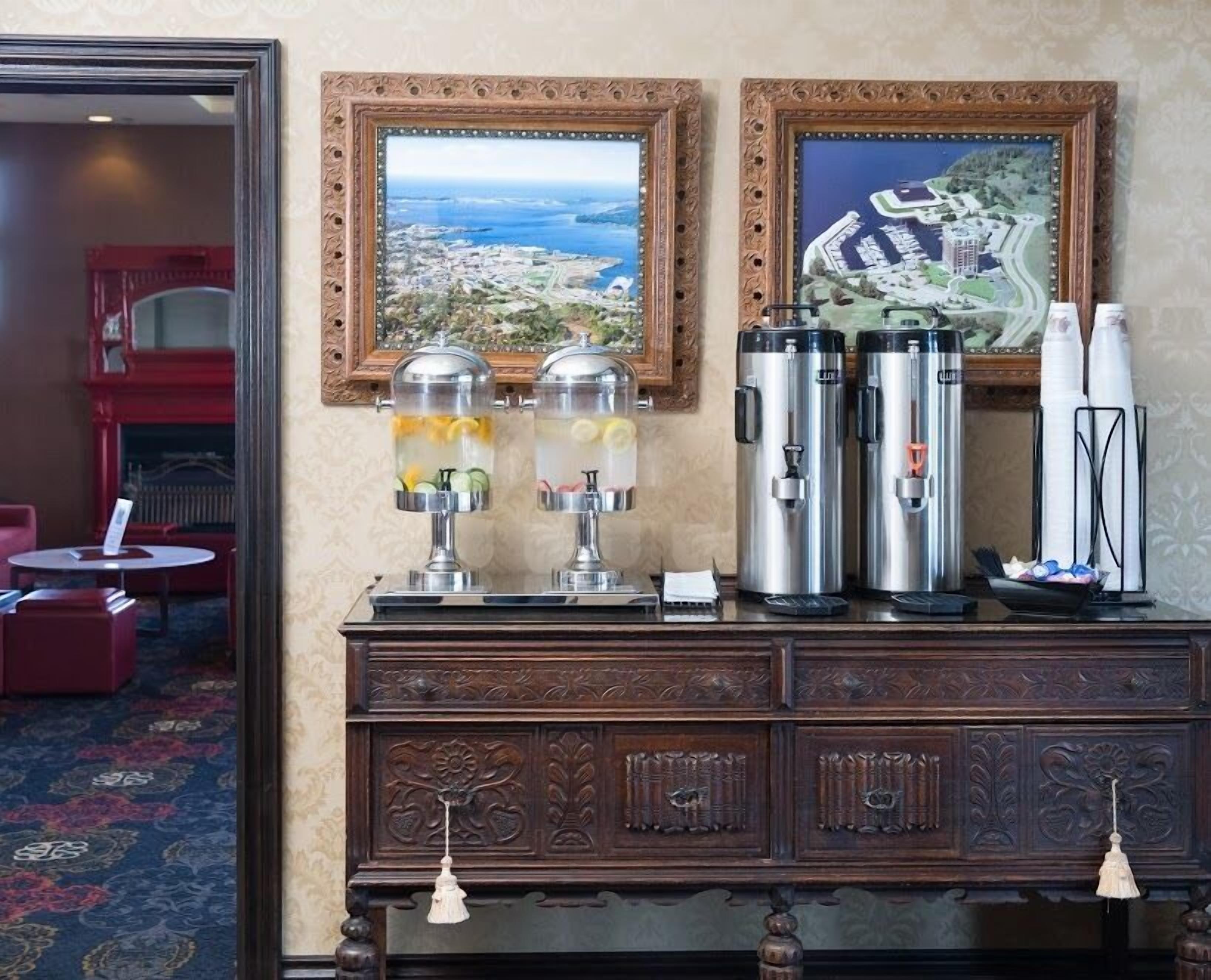 A hotel room with a wooden cabinet featuring two fruit-infused water dispensers, two stainless steel coffee makers, and a decorative hanging light.