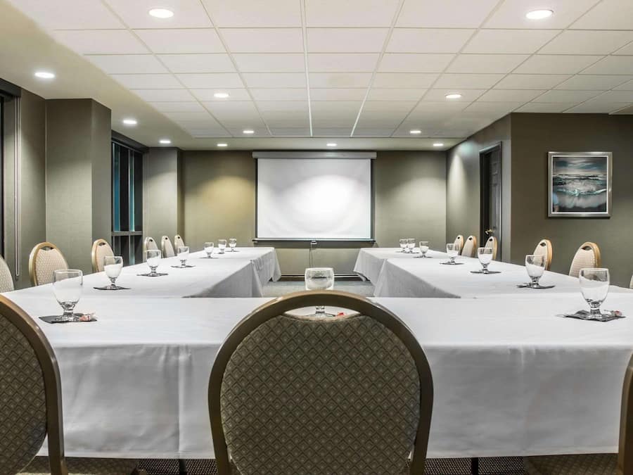 A conference room with two long tables, chairs, a projector screen, and a painting on the wall.