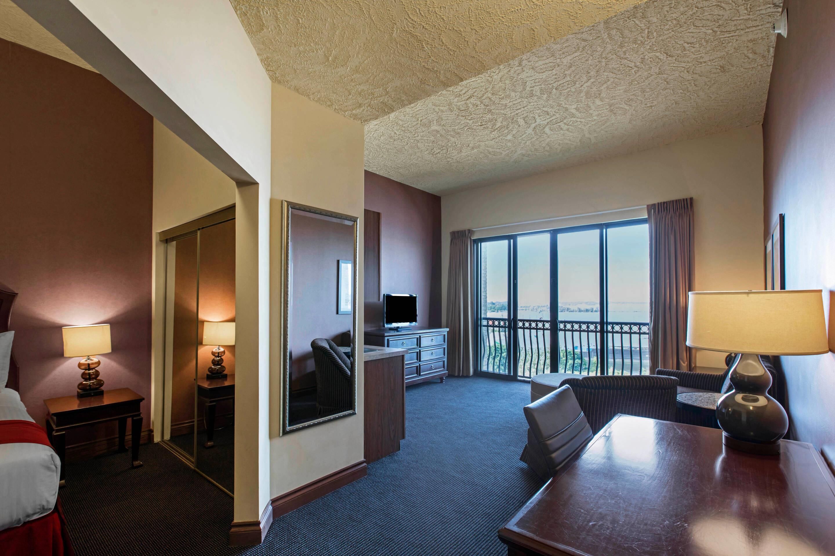 A hotel room with a bed, a desk, a TV, a dresser, and a balcony with a view.