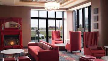 A room with a red sofa, two armchairs, a small table, and a fireplace. Large windows provide a view of the outside.