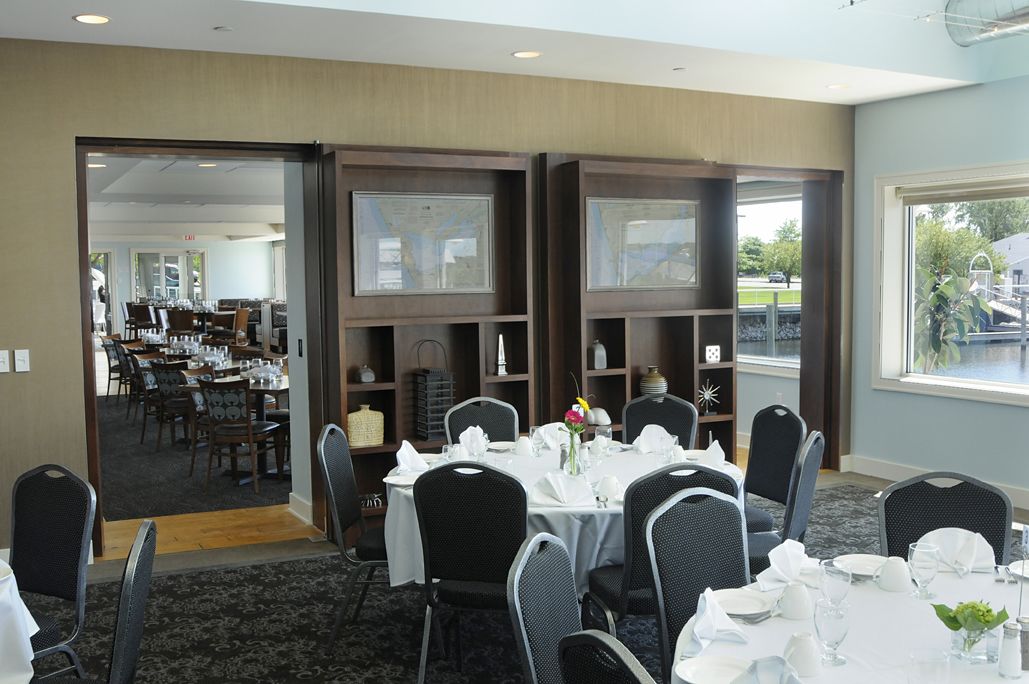 Un comedor con mesas dispuestas para una comida, vista del salón comedor a través de un ventanal y estantes con objetos decorativos.