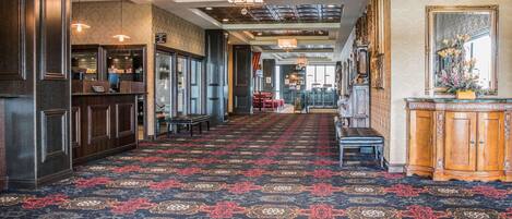 A hotel lobby with a patterned carpet, wooden furniture, and a bar area.