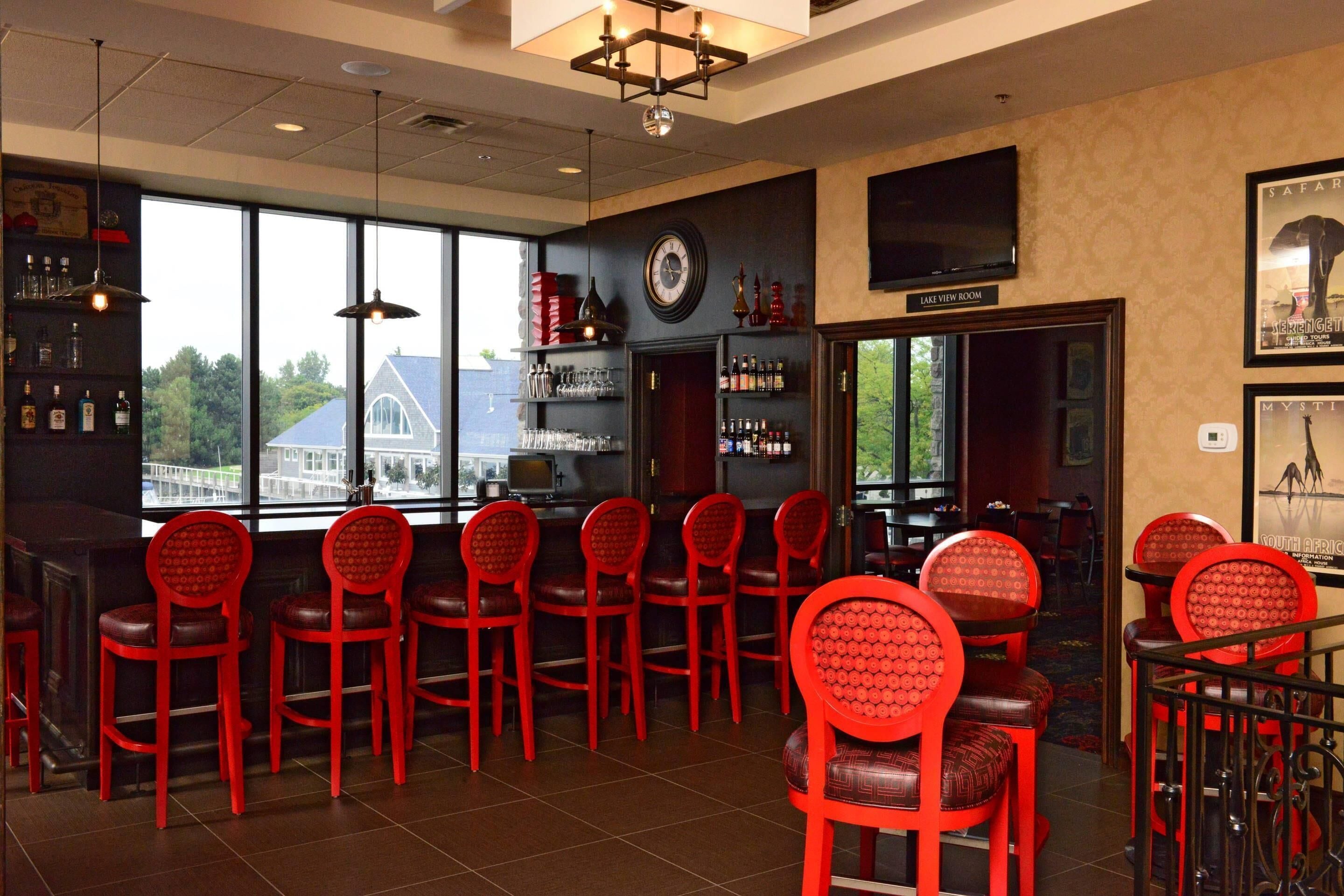 A bar area with red chairs, a clock, and a television mounted on the wall.