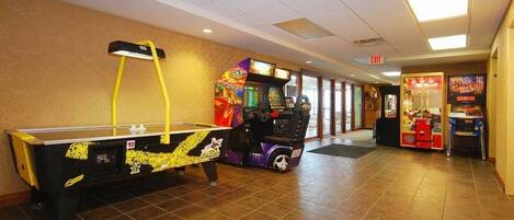 A hallway with a pool table, arcade games, and a vending machine.