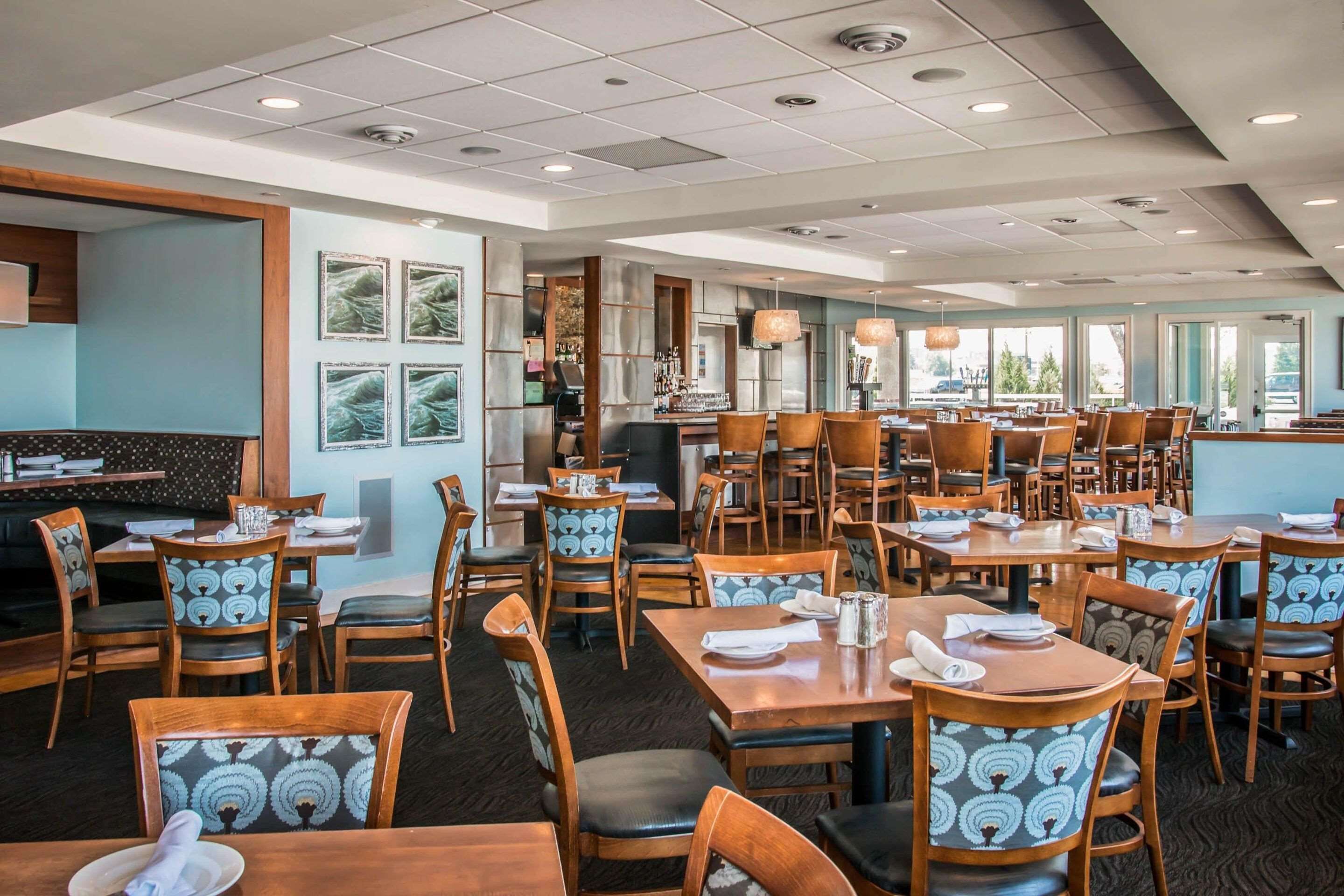 A spacious restaurant with wooden tables and chairs, a bar area, and framed artwork on the walls.