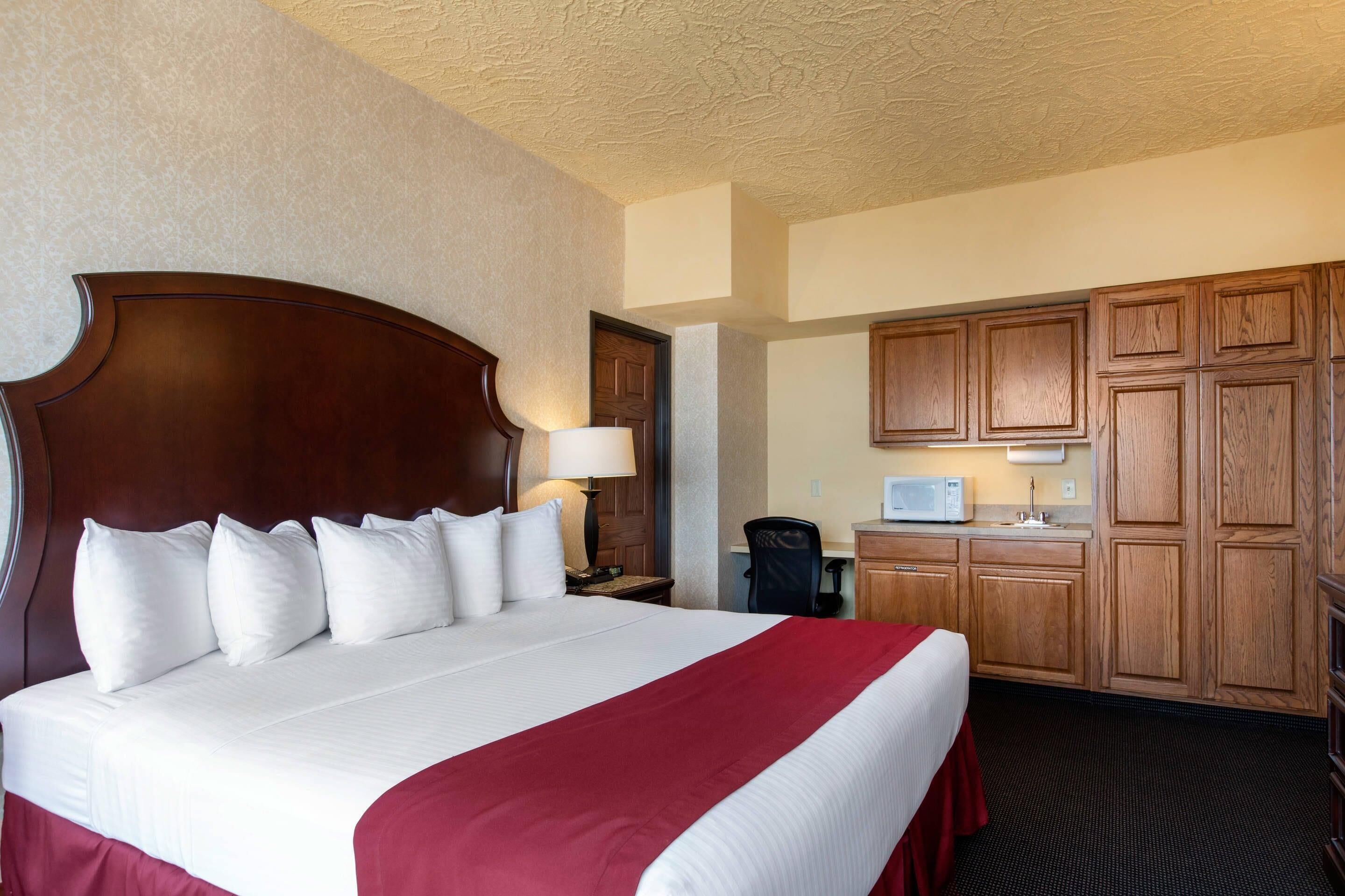 Ein Hotelzimmer mit einem großen Bett, einem Holz-Kopfteil, einem Schreibtisch mit Stuhl, einer Mikrowelle und Holzschränken.