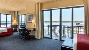 A hotel room with two beds, a desk, a chair, and a large window with a view of a body of water and a bridge.