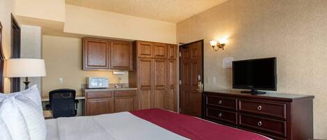 Quarto de hotel com uma cama grande, televisão, armários de madeira e uma kitchenette.