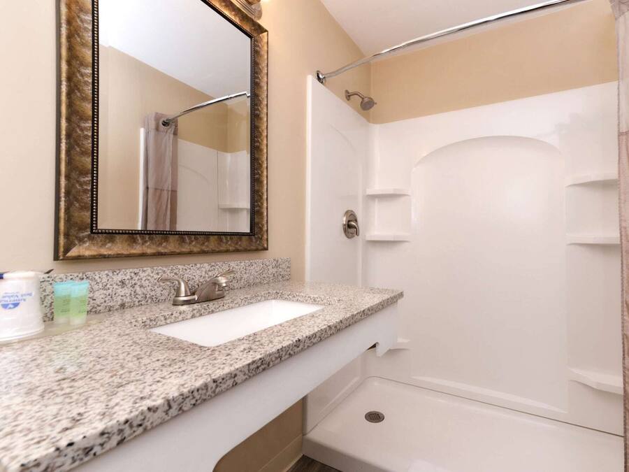 Un baño con encimera de granito, lavamanos, espejo, ducha y toallero.