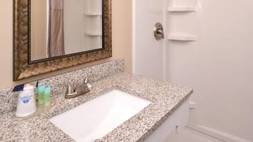 A bathroom with a granite countertop, a white sink, a mirror with a decorative frame, and a shower door.