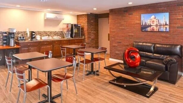 A modern living room with a black leather sofa, a coffee table with a red vase, and a dining area with wooden tables and chairs. - Motel 6 Putnam, CT (Putnam)