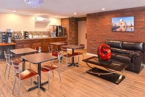 Un salon moderne avec un canapé en cuir noir, une table basse sur laquelle est posé un vase rouge, et un coin repas avec des tables et des chaises en bois.