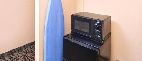 Una kitchenette pequeña con un microondas sobre un mueble negro, una tabla de planchar azul y un piso con diseño.