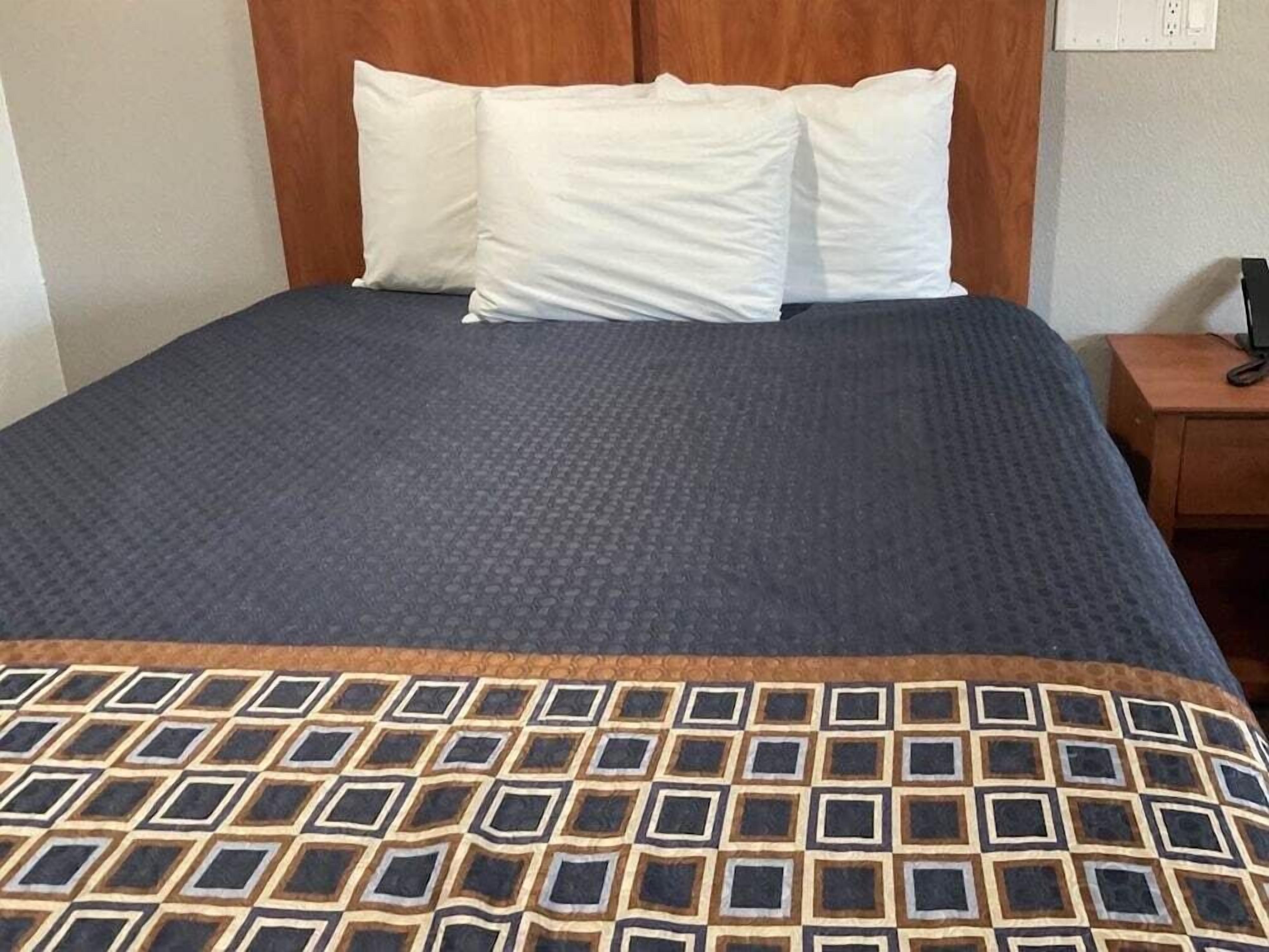 A bed with a patterned bedspread, a wooden headboard, and a bedside table with a phone.