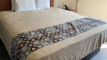 Ein ordentlich bezogenes Bett mit einem gemusterten Bettüberwurf, einem Kopfteil und einem Nachttisch mit einer Lampe.