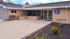 A building with a covered patio area, a bench, and a small garden. - Motel 6 Putnam, CT (Putnam)