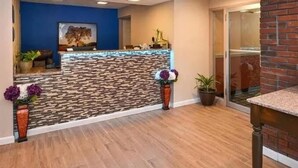 A reception area with a stone-patterned counter, potted plants, and a blue wall. - Motel 6 Putnam, CT (Putnam)