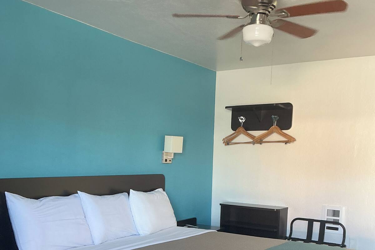 Un dormitorio con cama, ventilador de techo, lámpara de pared y perchero.