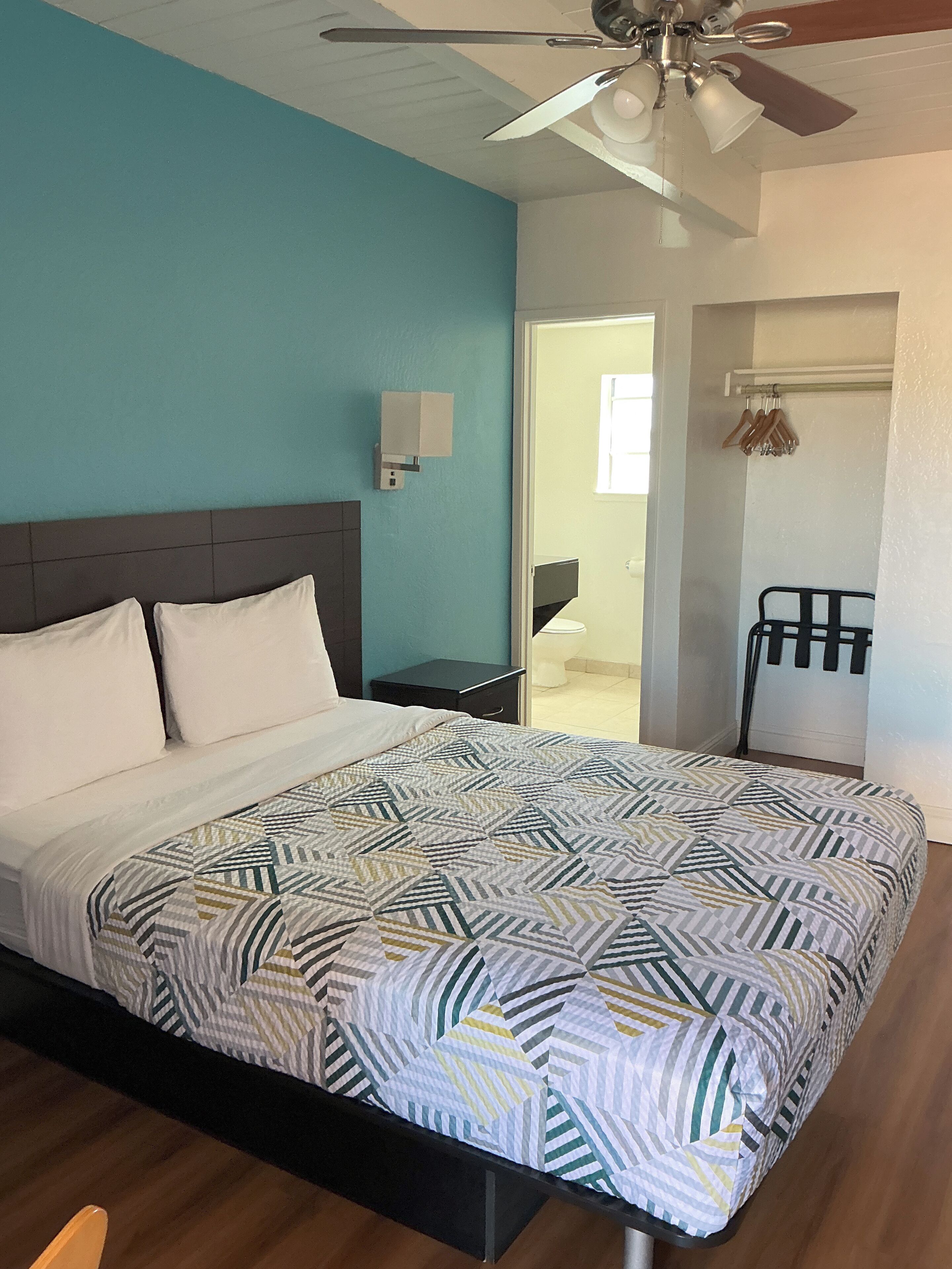 Une chambre à coucher comprenant un lit, un ventilateur de plafond, une table de chevet et une porte donnant accès à une salle de bain.