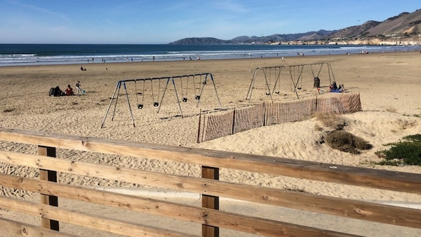 Una playa con cerca de madera, columpios y cielo despejado.