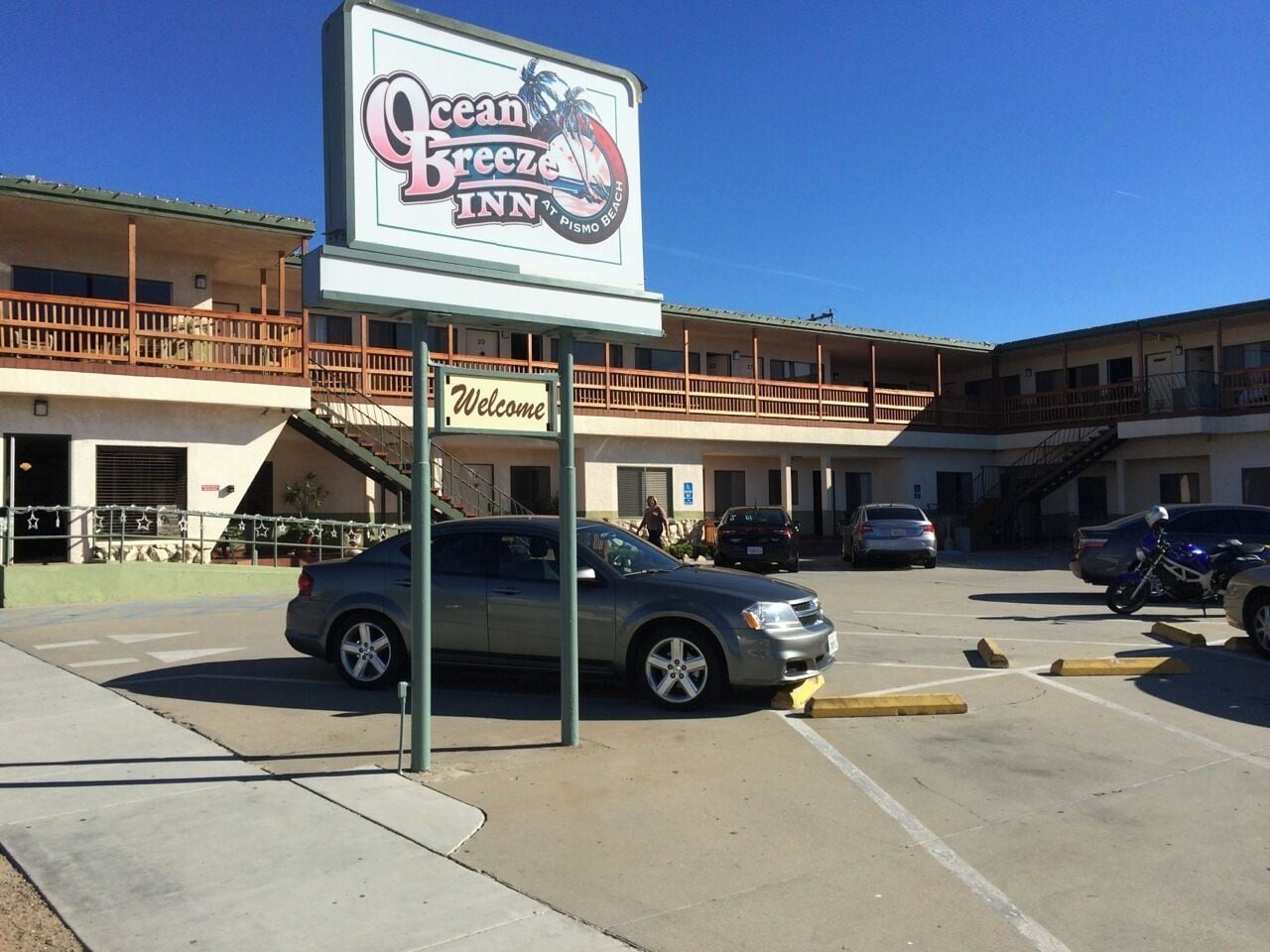 A building with a sign for Ocean Breeze Inn, a parking lot with cars, and a balcony with railings.