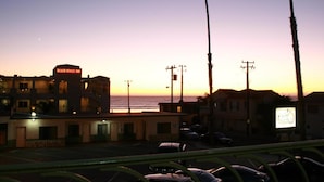 Una posada tipo casa de playa con un letrero, palmeras y vistas al atardecer.