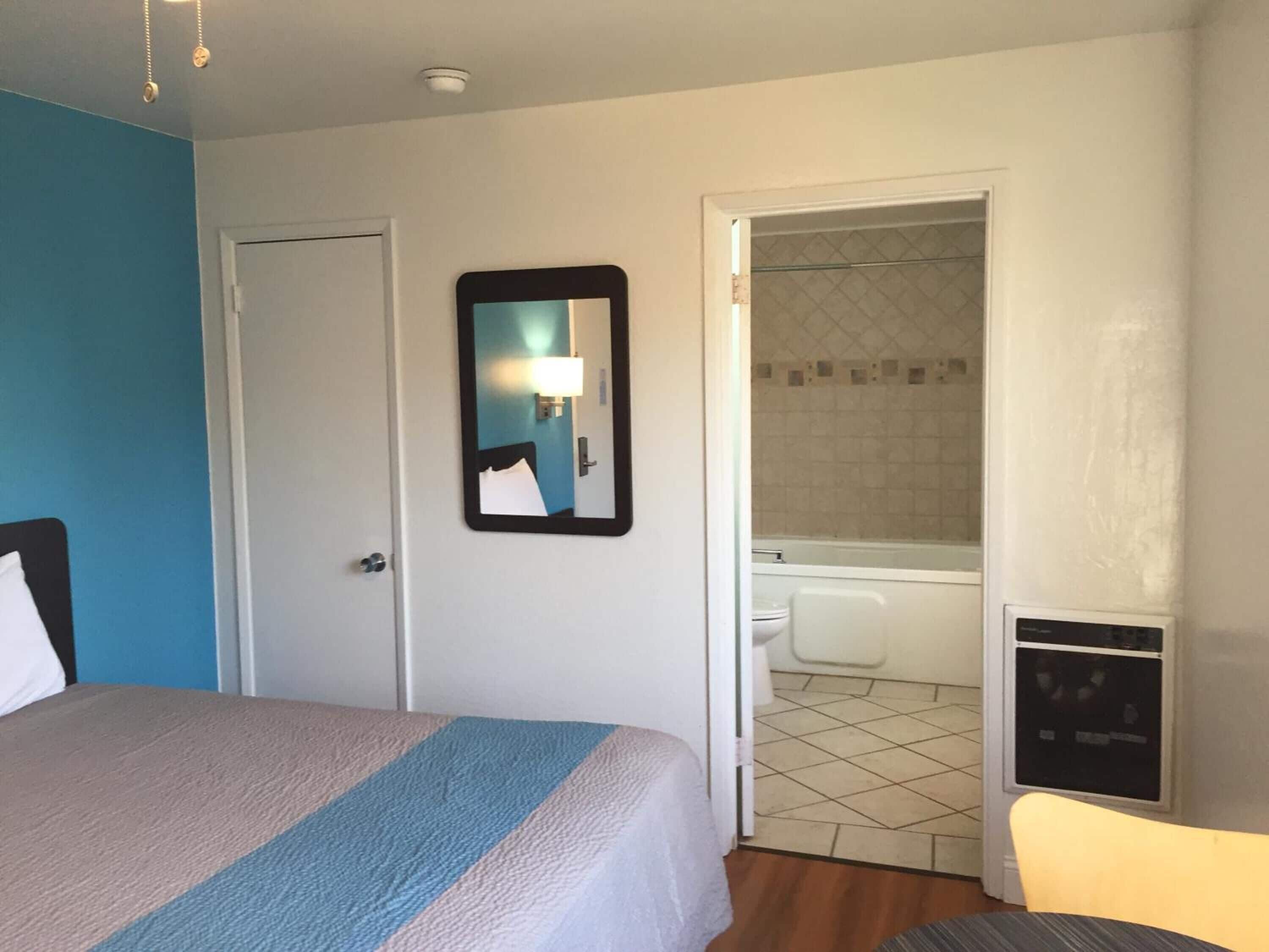 A hotel room with a bed, a bathroom visible through an open door, and a small table with a chair.