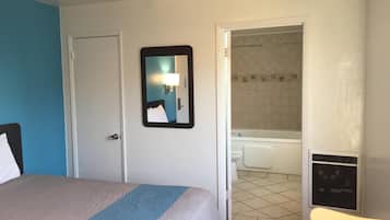 A hotel room with a bed, a bathroom visible through an open door, and a small table with a chair.
