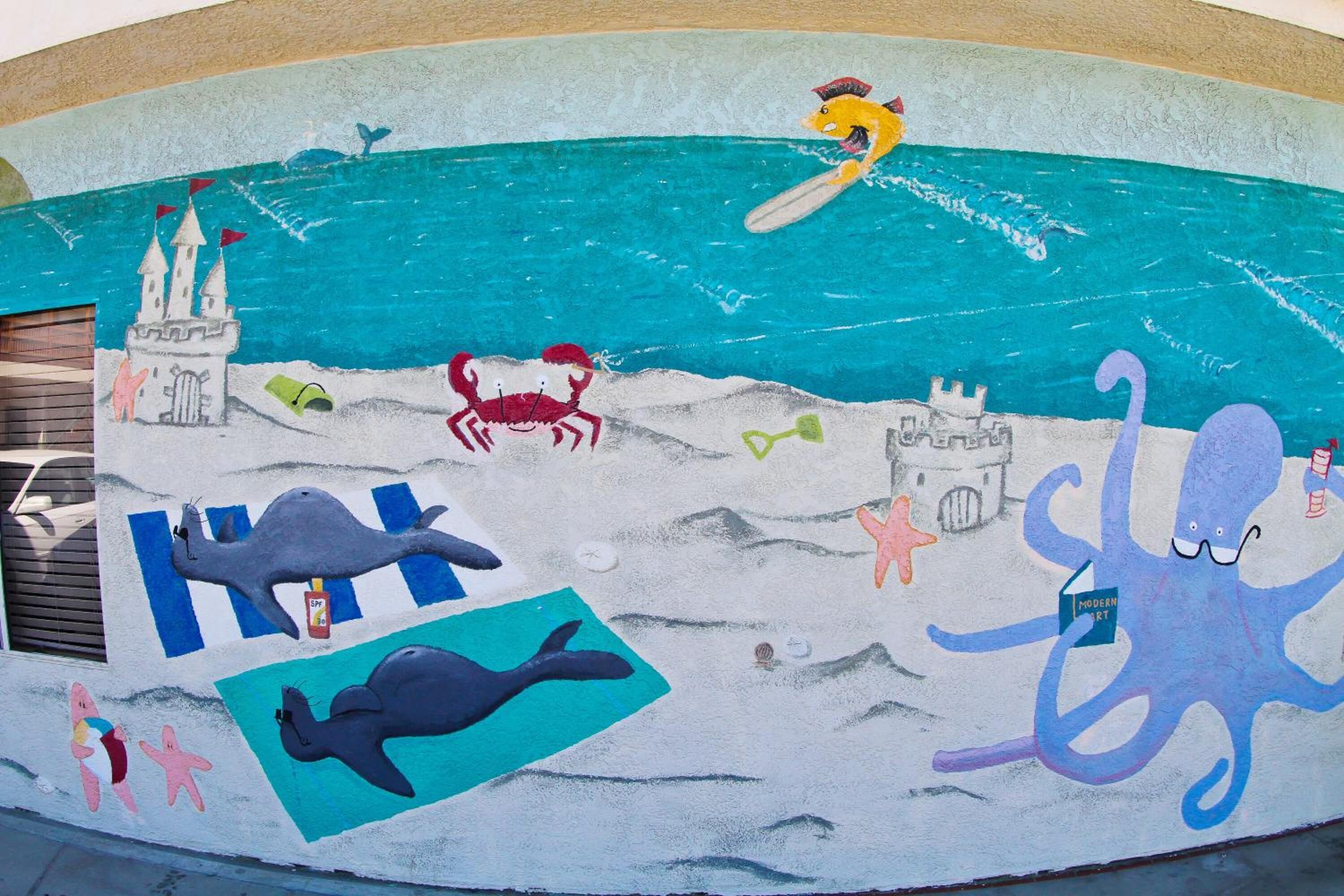 A mural with a castle, a whale, a crab, and an octopus on a beach scene.