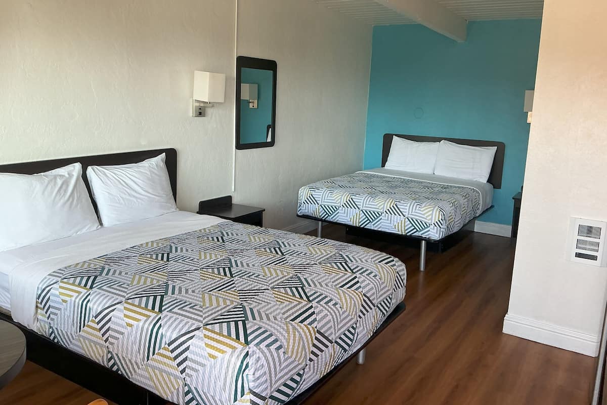 Habitación de hotel con dos camas, una mesita de noche, un espejo y un aire acondicionado instalado en la pared.