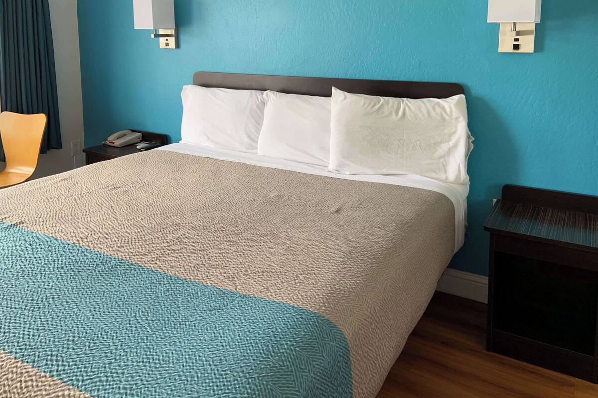 Una habitación de hotel con una cama grande, una mesita de noche con un teléfono y otra mesita junto a la cama.