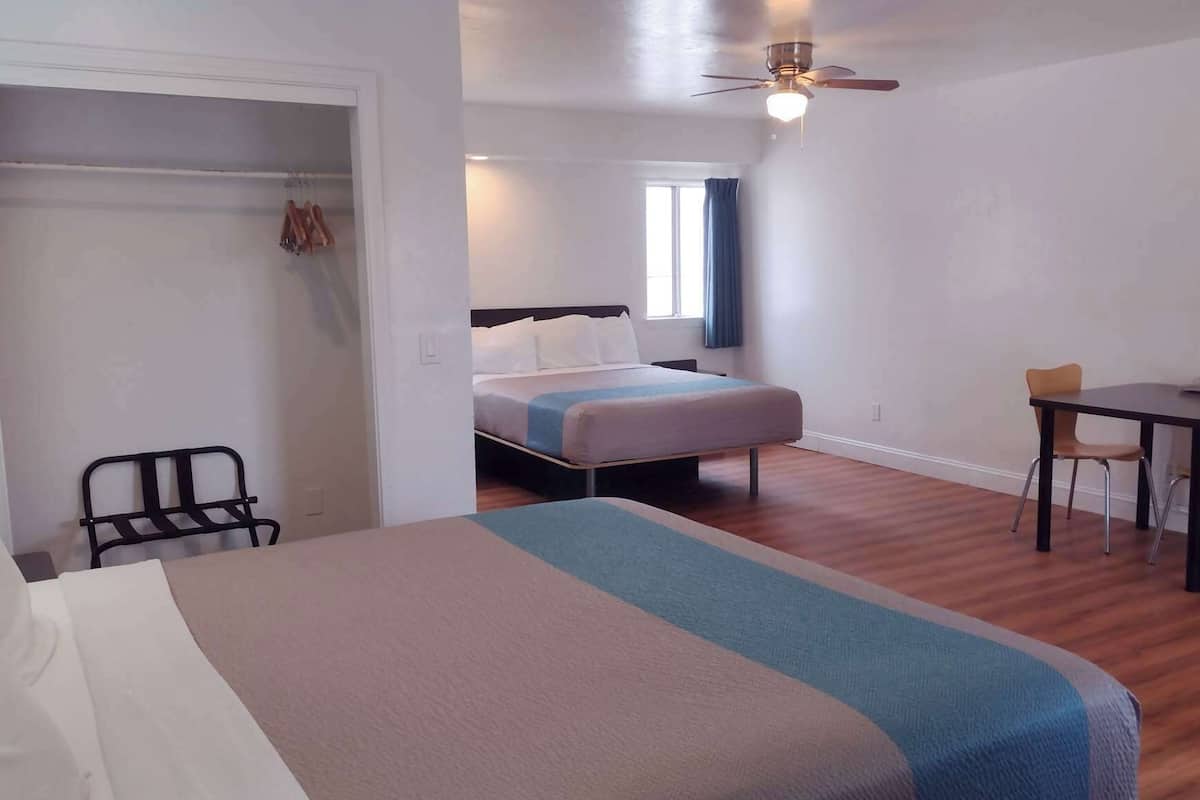 Una habitación de hotel con una cama, un escritorio con dos sillas, un armario y un ventilador de techo.