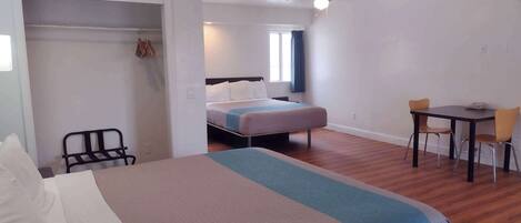 A hotel room with a bed, a desk with two chairs, a wardrobe, and a ceiling fan.