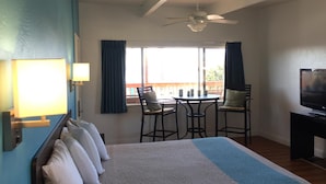 Habitación de hotel con cama, escritorio con televisor, ventilador de techo, ventana con cortinas y vista al exterior.