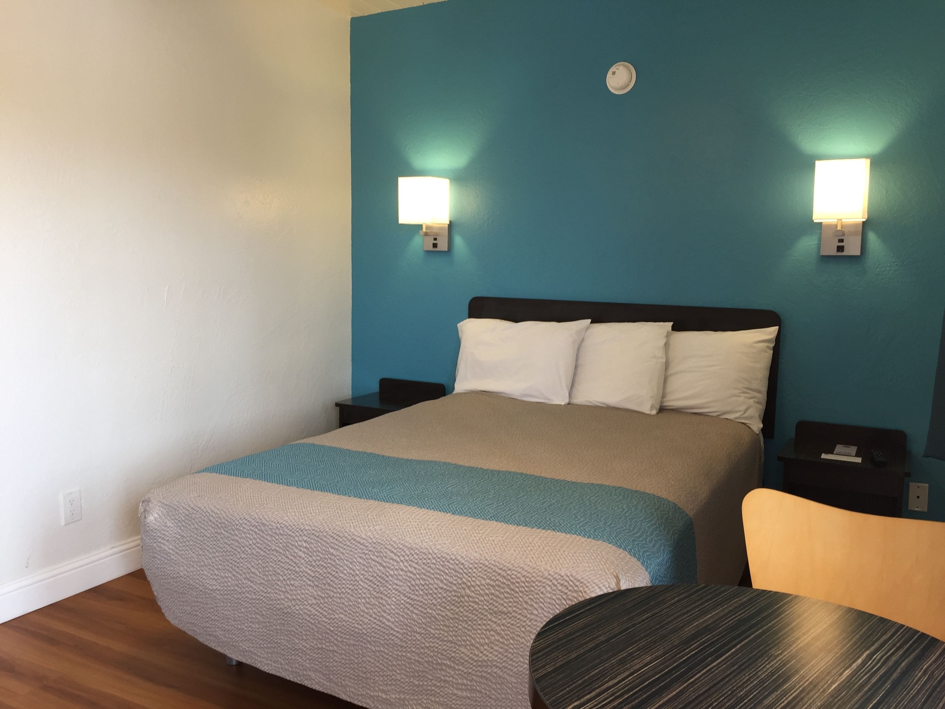 A hotel room with a bed, bedside tables, a chair, and wall-mounted lights.