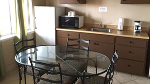 Una cocina compacta con una mesa de vidrio, sillas, microondas, cafetera y refrigerador.